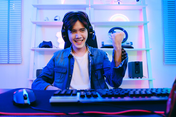 Portrait of Asian male gamer celebrating victory in front of the gaming table. Gamer winning an esports game with victory emotion. The player rejoices in victory in the competition.