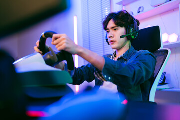 Asian male pro gamer playing an online car drive simulation game with steering wheel controller. Gamer focus an sports game with concentrate emotion. The player rejoices in victory in the competition. © artitwpd