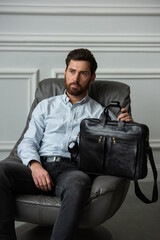 A man is comfortably sitting in a chair, resting with a leather briefcase near him