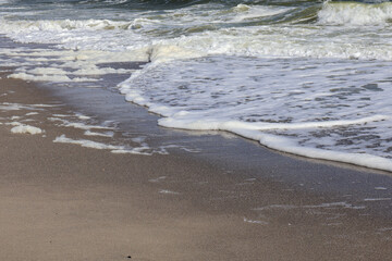 Sea Foam on a Sandy Beach. Close-up of gentle waves leaving a trail of sea foam on a sandy shoreline, showcasing the textures and serenity of the coastal landscape.