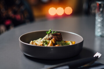 Gourmet dish in focus, featuring grilled meat with garnish in a ceramic bowl. Close-up composition...