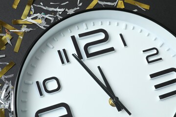 Big beautiful stylish clock showing five to twelve with confetti on black background 