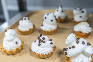 Shortcrust pastry tartlets with fluffy white cream or cream, decorated with chocolate on a tray on the production table, in a pastry shop or workshop.