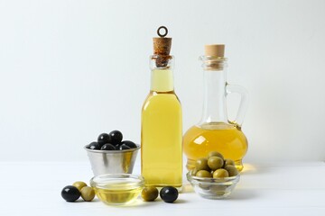 Bottles of fresh olive oil and olives with leaves on white background