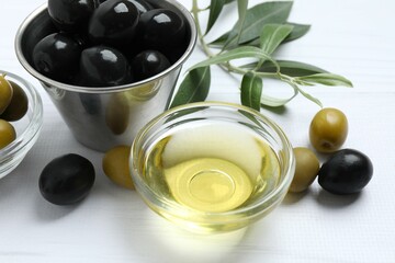 Bowl of fresh olive oil and olives with leaves on wooden background