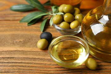 Bowl of fresh olive oil and olives with leaves on wooden background