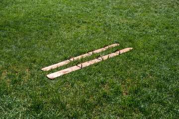 Wooden team-building skis on a grassy field under sunlight. Symbolizing outdoor activities, teamwork, and recreational games in natural settings.