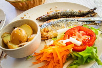 Grilled Sardines with Roasted Potatoes and Fresh Vegetable Salad Featuring Tomato, Carrots, and Lettuce on a Rustic Plate for a Mediterranean Culinary Experience