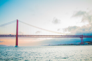 Scenic View of Iconic Suspension Bridge Over Tranquil Waters With Misty Skyline in the Background at Sunset, Showcasing Architectural Marvel and Serene Atmosphere in an Urban Setting