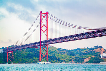 Iconic Red Bridge Spanning Across Tranquil River Against Lush Green Hills and Cloudy Sky Captures Tranquility and Majestic Engineering of Coastal Region