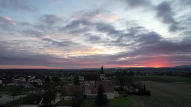 A peaceful village near Beaune awakens under a stunning sunrise, with the church spire standing tall against vibrant skies, embodying the charm of Burgundy's rural landscapes