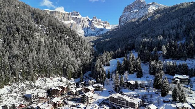 Canazei, Italy: Aerial view of ski resort in snowy Dolomites. Charming town landscape with chalets and hotels surrounded by snow-capped peaks, sunny day, clear blue sky
