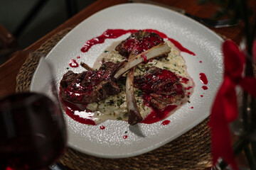 lamb chop stick grilled with red cherry sauce setted with porridge and topped with seasonal herbs, served with red wine in restaurant on wooden table