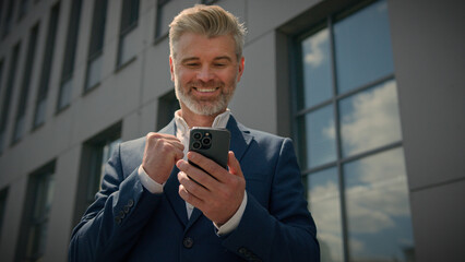 Caucasian happy old senior middle aged employer man mature businessman with phone achievement receive good news offer business success win excited overjoyed lucky smartphone rejoice bet victory city