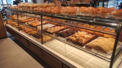 A well-organized bakery display featuring a variety of bread and pastries neatly packed in plastic wraps, showcased in glass shelves inside a bakery shop.