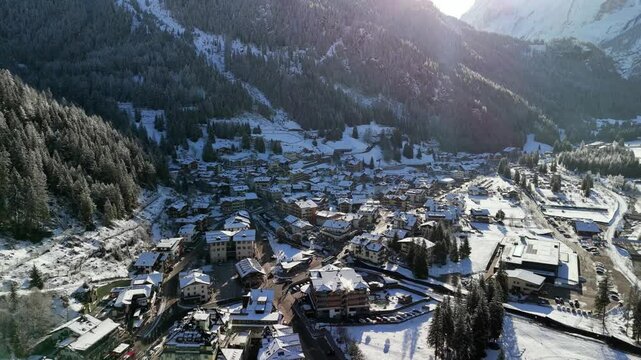 Canazei, Italy: Aerial view of ski resort in snowy Dolomites. Charming town landscape with chalets and hotels surrounded by snow-capped peaks, sunny day, clear blue sky
