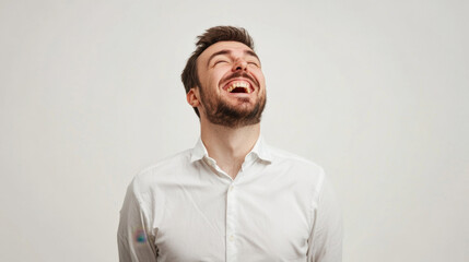 Obraz premium Caucasian male in a white shirt laughs joyfully against a plain background.