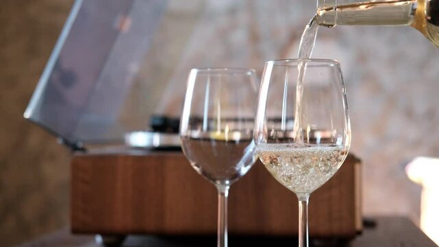 Pouring white wine into a glass from a bottle for cozy aperitif at home on the background of a record player