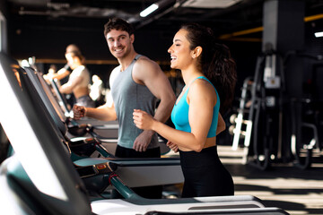 Athletic young people jogging on treadmills in gym, man and woman running, exercising together