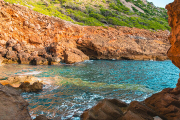 Scenic View of Rugged Rocky Coastal Landscape with Crystal Clear Blue Water and Lush Greenery on Hillside Under Bright Sunlight