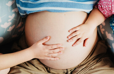 Little children holding hands on pregnant belly of mom. Pregnant woman in bed.