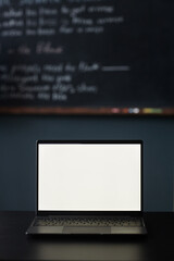 Vertical shot of laptop with mock up white screen displaying blank page resting on desk in classroom, copy space