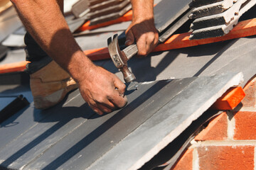 Roofing contractor installing shingles on a residential building under clear blue sky