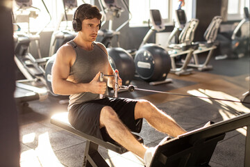 Plakat Focused man training hard in gym and pulling weights in seated cable row machine, wearing headphones and listening music