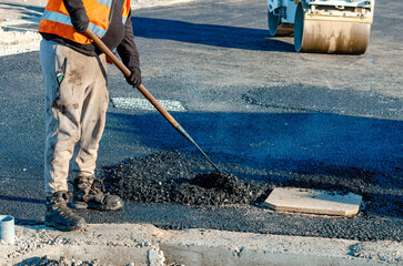 Road repair worker fills pothole with fresh asphalt during daytime construction in a city