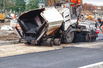 Asphalt paving machine laying down fresh asphalt on a busy road during daylight hours
