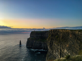 Naklejka premium Cliffs of Moher at sunset, featuring warm hues in the sky and a calm, serene ocean.