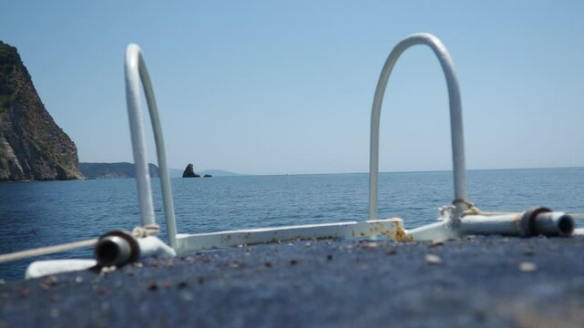 Calm waters stretch endlessly under a clear blue sky. Boat foreground showcases worn details while distant hills create tranquil backdrop. RT Dubovica Rocks near Buljarica, Svetac Rock, Montenegro.