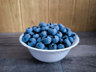 Fresh large blueberries in a white plate, on a brown background, on a gray table.
