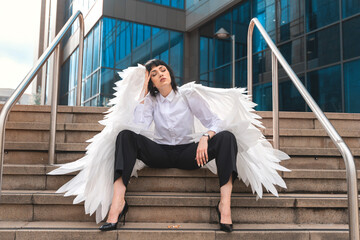 Stylish model poses with angelic wings on urban stairs in modern city setting during daylight