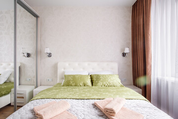 A well-appointed small modern bedroom with a cozy design, featuring a queen-sized bed, bedside tables. A large window with curtains allowing soft daylight.
