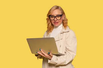 Professional woman with laptop against vibrant yellow background in modern setting