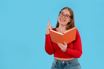 Young woman smiling while holding orange book against bright blue background during a reading session