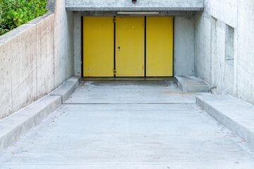 Driveway down to underground garage with yellow entrance door. Concrete floor and walls.