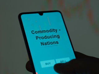 An investor analyzing the commodity - producing nations etf fund on a screen. A phone shows the...