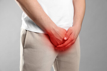STD (sexually transmitted diseases). Man holding hands near his groin on grey background, closeup