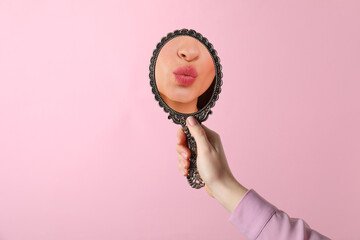 Beautiful woman looking in handheld mirror on pink background, closeup