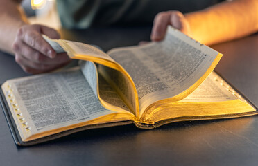 Naklejka premium A man reads the Bible. Male hands on the Holy Bible. Close-up of the Bible.