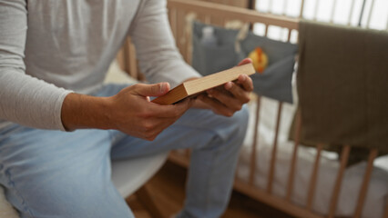 Young hispanic man holding a photo while sitting in a bedroom with a crib, capturing a thoughtful moment in an intimate home setting.