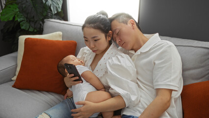 Obraz premium Woman holds phone while husband and baby sleep on couch in cozy living room scene, conveying family togetherness and modern lifestyle indoors.
