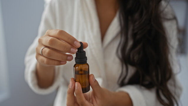 Young hispanic woman with brunette hair holding a dropper bottle in a wellness center or spa room focusing on her hands and the product