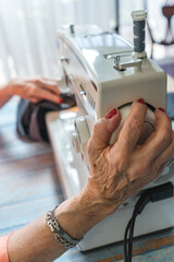 Hands of a eldlerly seamstress sewing a pair of pants on a sewing machine.