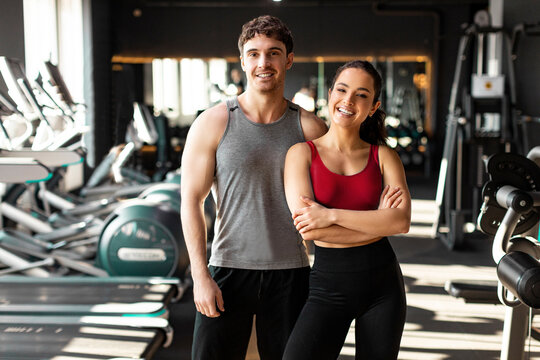 Happy strong fitness couple, man and woman, standing in modern gym and smiling at camera while having break during training