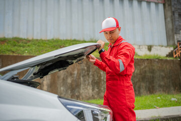 A mechanic inspects a vehicles engine compartment while wearing a bright red jumpsuit