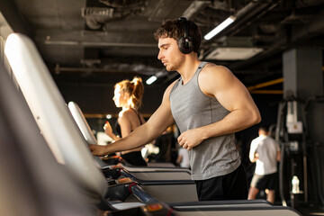 Fototapeta premium European sportsman adjusting speed on treadmill while running, working out and listening music in gym interior
