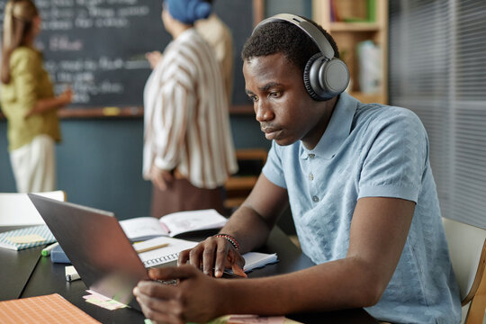 Concentrated African American male student in headphones using laptop completing listening task in English class at language school for adult learners, copy space